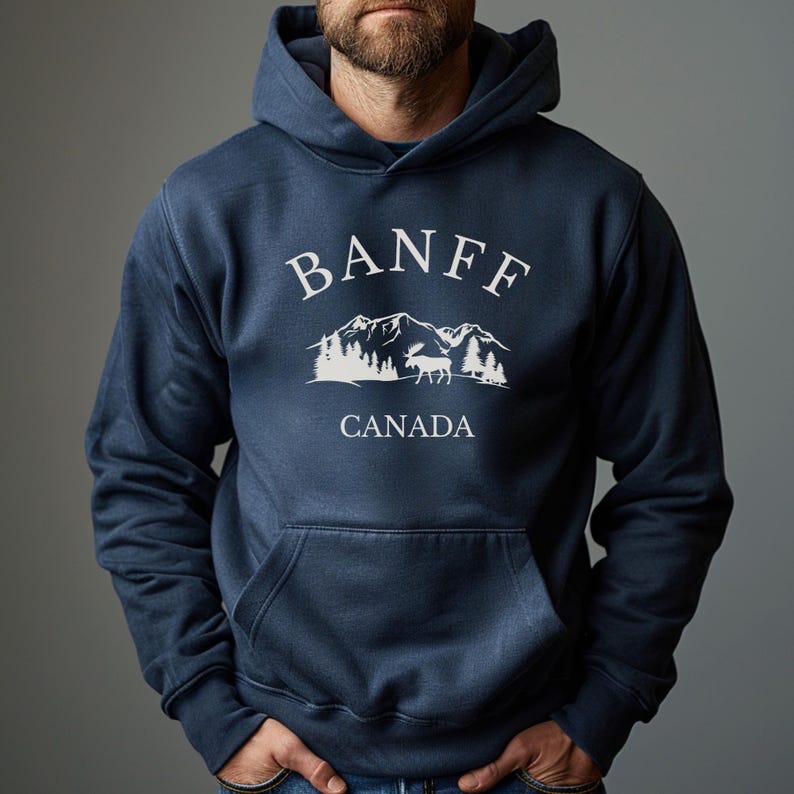 A man wearing a navy blue hoodie with a dark grey graphic that reads BANFF CANADA above an illustration of mountains, trees, and a moose.