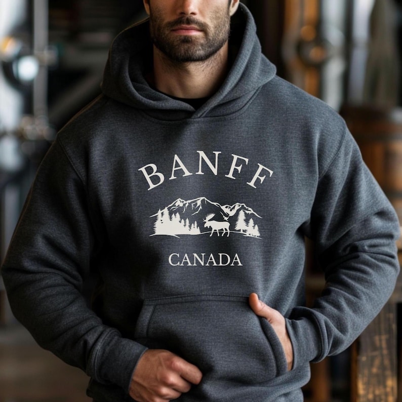 A man wearing a dark grey hoodie with a white graphic that reads BANFF CANADA above an illustration of mountains, trees, and a moose.