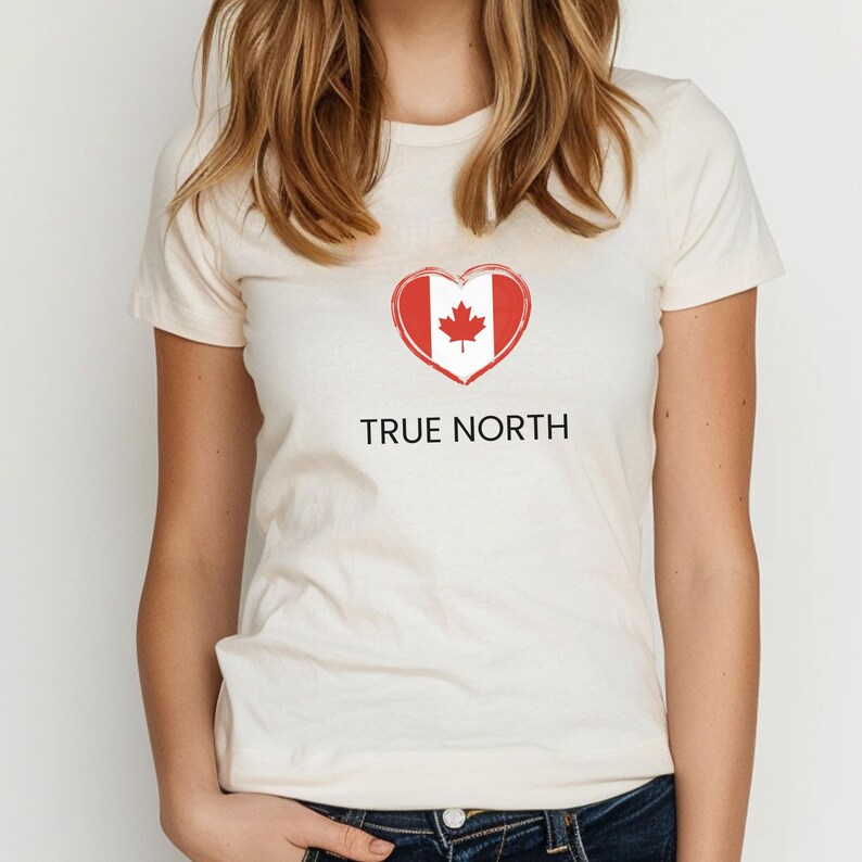A woman wearing a cream coloured slim-fit t-shirt featuring a True North design with a heart-shaped Canadian flag graphic in red and white. The t-shirt has a flattering fit and short sleeves.