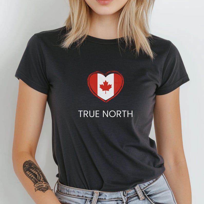 A woman wearing a black slim-fit t-shirt featuring a True North design with a heart-shaped Canadian flag graphic in red and white. The t-shirt has a flattering fit and short sleeves.