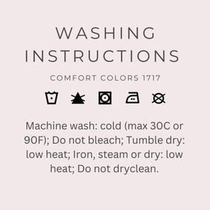 May include: A light pink graphic card displaying WASHING INSTRUCTIONS for Comfort Colors 1717. It features five black laundry symbols and text: Machine wash: cold (max 30C or 90F); Do not bleach; Tumble dry: low heat; Iron, steam or dry: low heat; Do not dryclean.