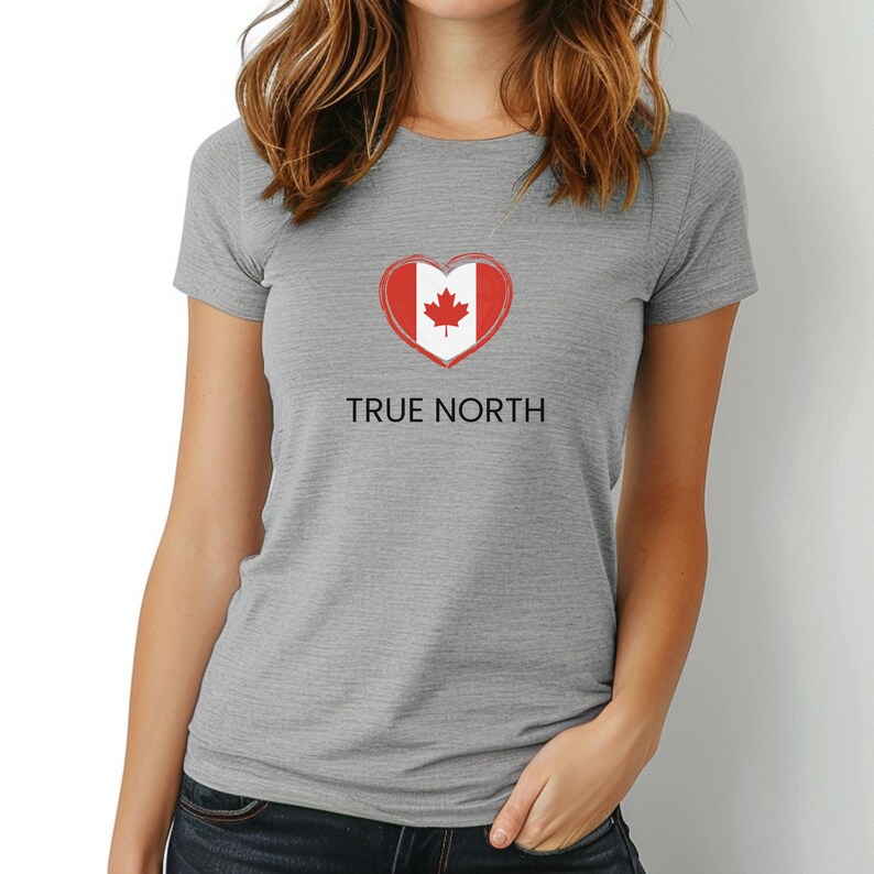 A woman wearing a grey slim-fit t-shirt featuring a True North design with a heart-shaped Canadian flag graphic in red and white. The t-shirt has a flattering fit and short sleeves.