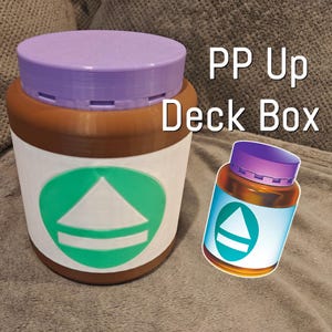 May include: A large, cylindrical container with a purple lid and a brown base, labeled "PP Up Deck Box." The container has a white label with a green and white graphic. A smaller, similar container is also present.