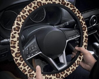 Peut inclure: Housse de volant à imprimé léopard. Le couvercle présente un fond beige avec des taches marron et une bordure noire. L'image montre le couvercle installé sur le volant d'une voiture.