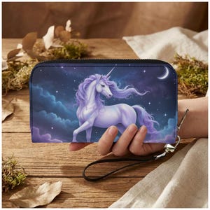 May include: A black zip-around wallet featuring a majestic white unicorn with flowing purple mane and tail, set against a starry night sky with a crescent moon. The wallet has a wrist strap.