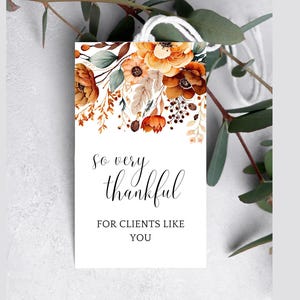 Op de afbeelding: Een witte kaart met een bloemenontwerp in tinten oranje, bruin en groen. De tekst op de kaart luidt "So very thankful for clients like you."