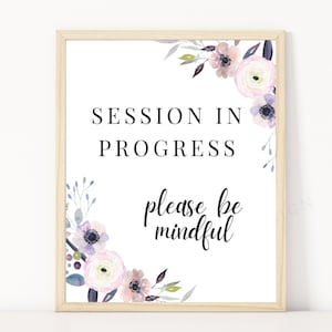Puede incluir: Un cartel blanco con marco de madera y detalles florales morados. El cartel dice "Sesión en curso, por favor, sea consciente".