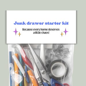 May include: A clear plastic bag filled with various office and craft supplies, including pens, scissors, tape, and paper clips. The bag is topped with a white card that reads "Junk drawer starter kit" in blue and purple text.