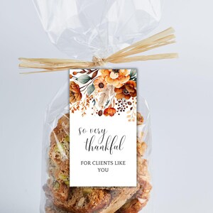 Op de afbeelding: Een wit cadeau-etiket met een bloemenontwerp in tinten oranje, geel en bruin. Het etiket zegt "So very thankful for clients like you".