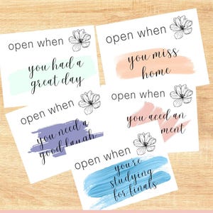 May include: Five white cards with black script and watercolor accents. Each card reads "open when" followed by a different sentiment: "you had a great day," "you miss home," "you need a good laugh," "you aced an assignment," and "you're studying for finals."