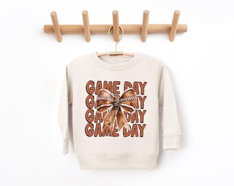 May include: A cream coloured sweatshirt with a brown football bow and the text "GAME DAY" repeated four times.