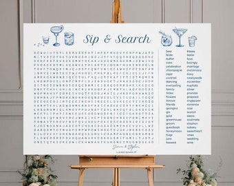 May include: A white sign with blue text and illustrations of cocktails. The sign says "Sip & Search" and has a word search puzzle with wedding-related words. The sign is on an easel in front of a white wall with a floral arrangement on either side.