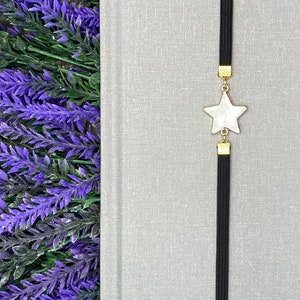 May include: A black elastic bookmark with a white star charm. The bookmark is hanging from a gray notebook.