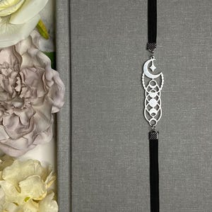 May include: A silver bookmark with a moon and stars design, hanging from a black tassel. The bookmark is attached to a gray book cover.