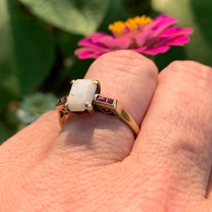 May include: A gold ring with a white opal gemstone and red ruby accents.