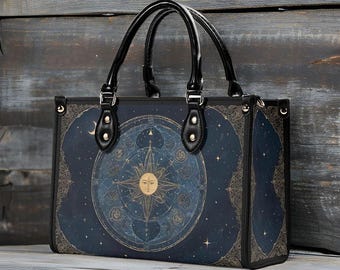 May include: A tote bag with a celestial design. The bag features a dark blue background with a gold sun, stars, and astrological symbols. It has black handles and trim, and is made of a durable material.