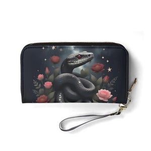 Könnte beinhalten: Schwarze Geldbörse mit Reißverschluss und Handschlaufe. Sie zeigt eine detaillierte Illustration einer grauen Schlange mit roten Augen, umgeben von rosa und roten Rosen, vor einem dunklen Sternenhimmel. Ca. 20 cm lang.