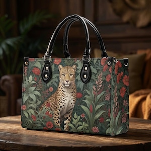 May include: A rectangular handbag featuring a leopard amidst a floral design with red flowers and green foliage. The bag has black handles and accents. The bag is sitting on a wooden surface.
