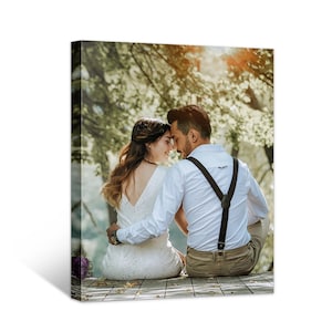 May include: A bride and groom in a forest setting, the bride is wearing a white dress and the groom is wearing a white shirt and brown pants with suspenders. They are looking at each other and smiling.