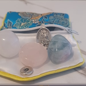 May include: A small blue satin pouch with a zipper closure containing three smooth, polished stones: a white selenite, a pink rose quartz, and a blue-green aquamarine. A silver charm with the inscription "Guardian Angel" hangs from the zipper pull.