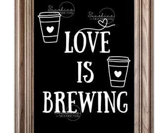 May include: A framed print with a black background and white text that reads "LOVE IS BREWING." The image includes two coffee cup illustrations with hearts and the text "Sunshine and Moonbeams" in a circular design. The frame is a light brown color.