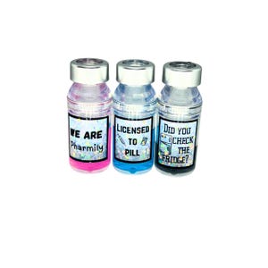 three different liquid vial caps. pink liquid vial cap says we are pharmily, blue liquid vial cap says licensed to pill, gray liquid  vial cap says "did you check the fridge?"