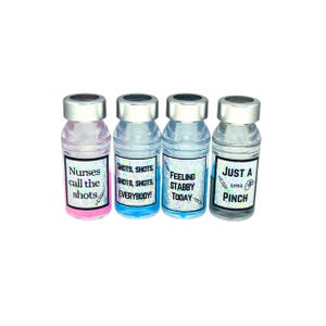 four different liquid vial caps. pink liquid vial cap says nurses call the shots, blue liquid vial cap says shots shots shots shots everybody, blue liquid vial cap says feeling stabby today, gray liquid  vial cap says just a little pinch