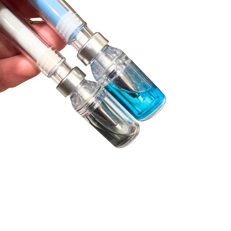 two pens with liquid vial caps held at an angle showing that the liquid is free flowing because the liquid has shifted inside the vial cap to match the angle