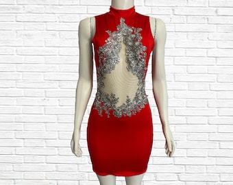Puede incluir: Un vestido rojo sin mangas con cuello alto y un panel transparente en la parte delantera. El panel transparente está decorado con lentejuelas plateadas y abalorios en forma de flores.