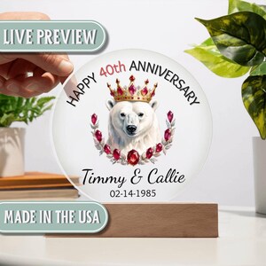 May include: A round, clear acrylic plaque with a polar bear wearing a crown, surrounded by red jewels. The plaque reads "Happy 40th Anniversary" and includes names and a date. It sits on a wooden base.