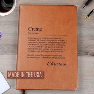 May include: A brown leather journal with the word "Create" and its definition printed on the cover. The journal has a personalized name at the bottom and the text "Made in the USA" is visible. A cup of coffee and a pen are next to the journal.