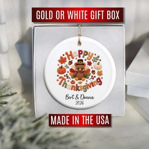 May include: A round white ceramic ornament featuring a colorful graphic of a turkey wearing a pilgrim hat surrounded by autumn leaves, pumpkins, and acorns. The text reads Happy Thanksgiving, Bert & Donna, and 2026. It is inside a gift box.