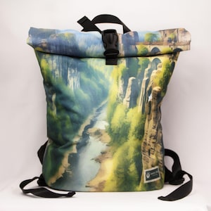 Könnte beinhalten: Ein Rolltop-Rucksack mit einem aufgedruckten Landschaftsmotiv, das einen Fluss zeigt, der sich durch eine felsige Schlucht mit grünen Bäumen schlängelt. Der Rucksack hat schwarze verstellbare Riemen, einen schwarzen Kunststoff-Schnallenverschluss und ein Etikett.