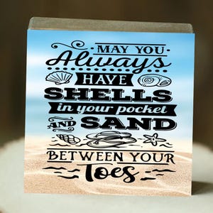 May include: A wooden sign with a beach scene background and the text "MAY YOU Always HAVE SHELLS in your pocket AND SAND BETWEEN YOUR Toes".