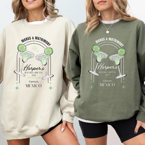 May include: Two sweatshirts, one sand-colored and one military green, feature a margarita graphic with the text "MARGS & MATRIMONY" and "Harper's BACHELORETTE 2025 Cancun, MEXICO". The design includes lime slices and star accents.