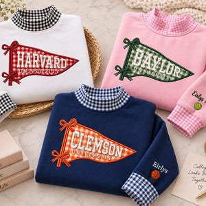 Peut inclure: Trois sweat-shirts à manches longues en blanc, rose et bleu marine. Chacun présente un col montant avec une bordure vichy, une applique en forme de fanion avec les noms d'université Harvard, Baylor ou Clemson, et une broderie personnalisée.