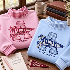 Könnte beinhalten: Ein rosafarbenes und ein hellblaues Sweatshirt, beide mit einem Stehkragen im Vichy-Karo-Muster. Jedes Kleidungsstück zeigt einen gestickten Buchstaben A mit Vichy-Füllung, einen Wimpel mit der Aufschrift ALPHA CHI und den Text EST. 1885 mit zwei Schleifen.