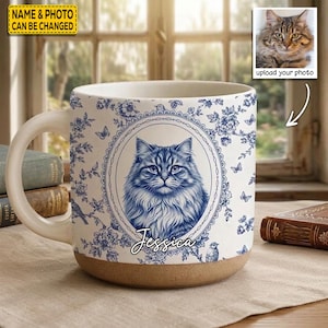 Könnte beinhalten: Ein Keramikbecher mit blau-weißem Blumenmuster und einem zentralen ovalen Rahmen, der das Porträt einer langhaarigen Katze zeigt. Der Name Jessica ist in Schreibschrift unter der Katze aufgedruckt. Der Becher hat einen naturfarbenen Boden.