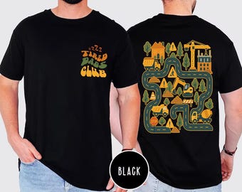 May include: Black t-shirt with the text "Tired Dads Club" on the front and a construction-themed graphic on the back. The graphic includes roads, trucks, trees, and a crane. The shirt is made of a soft material.