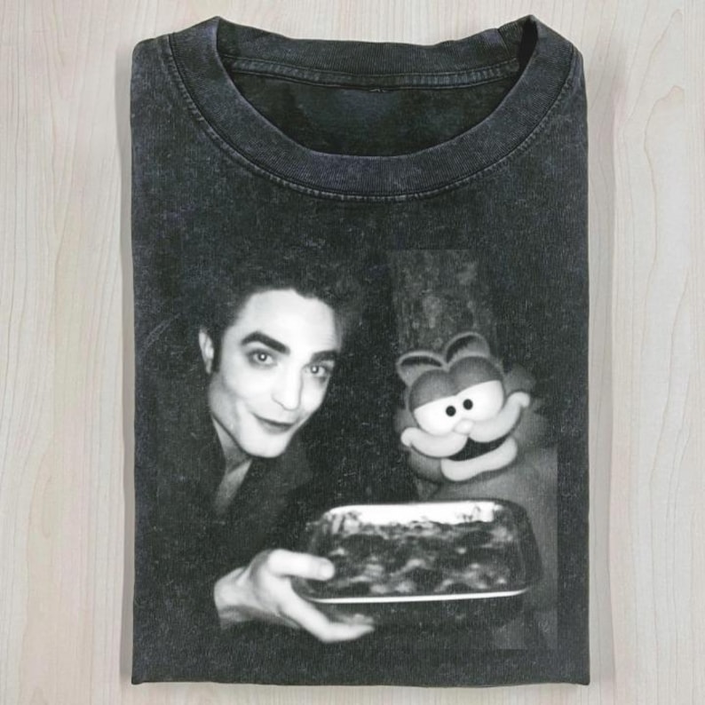 May include: Black and white graphic t-shirt featuring a vintage image of a man and a cartoon cat holding a dish. The t-shirt has a crew neck and short sleeves. The image is centered on the front of the shirt.