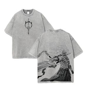 May include: Grey t-shirt with a black and white graphic. The front shows a sword in a circle, the back a detailed warrior illustration with a large sword. The shirt has short sleeves and a crew neck. The fabric has a washed effect.