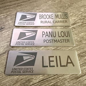 May include: Three rectangular name badges with the United States Postal Service logo. The badges display names and titles: Brooke Mullis, Rural Carrier; Panu Loui, Postmaster; and Leila.