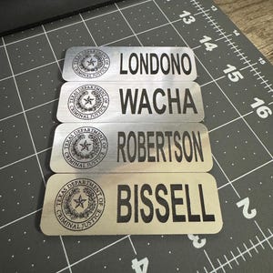 May include: Four silver name tags with black text and a black and white seal. The names on the tags are Londono, Wacha, Robertson, and Bissell.