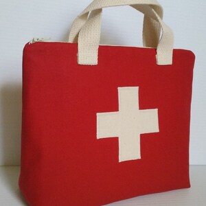 May include: A red first aid kit bag with a white cross emblem on the front. The bag has a zippered top and cream-colored handles. The bag is made of a sturdy material.