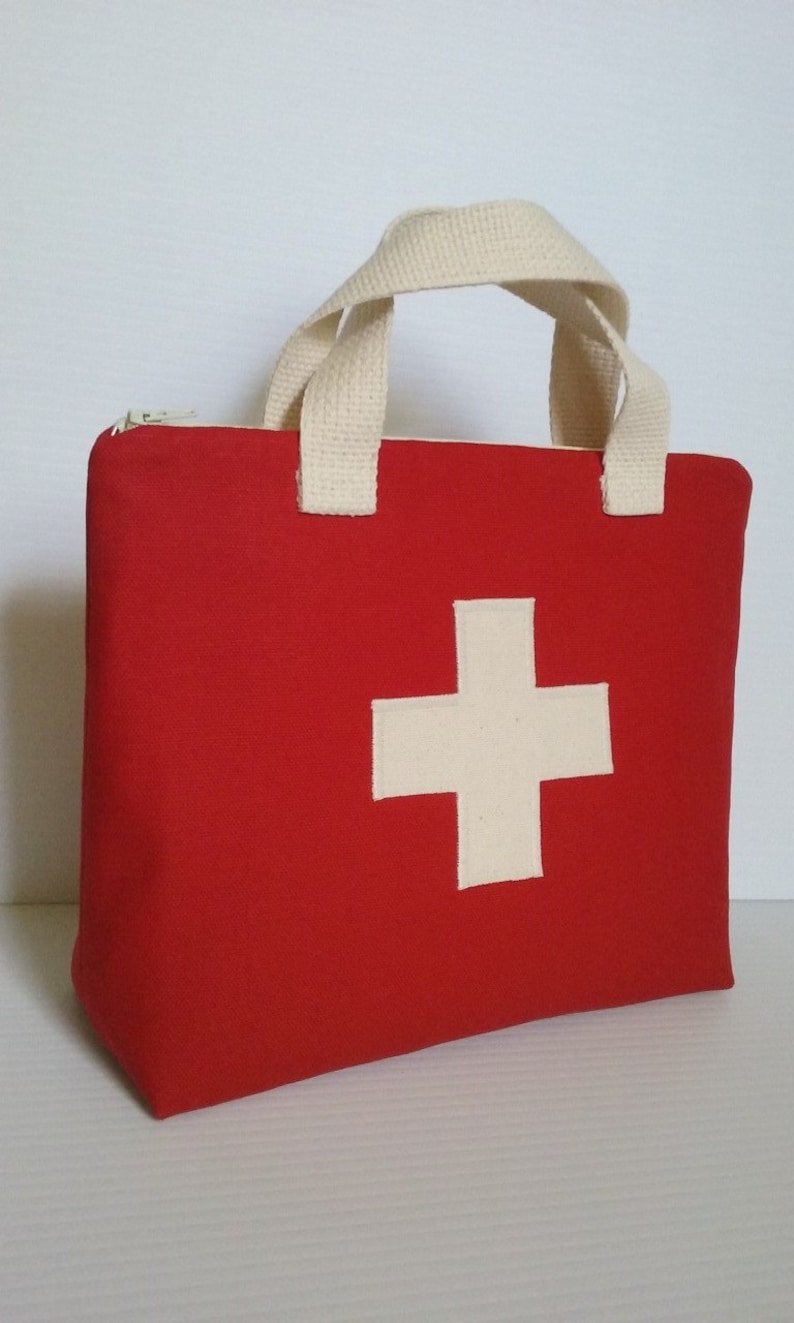 May include: A red first aid kit bag with a white cross emblem on the front. The bag has a zippered top and cream-colored handles. The bag is made of a sturdy material.