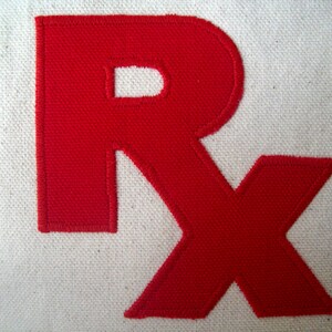 May include: Red fabric letters "RX" sewn onto a white canvas background.