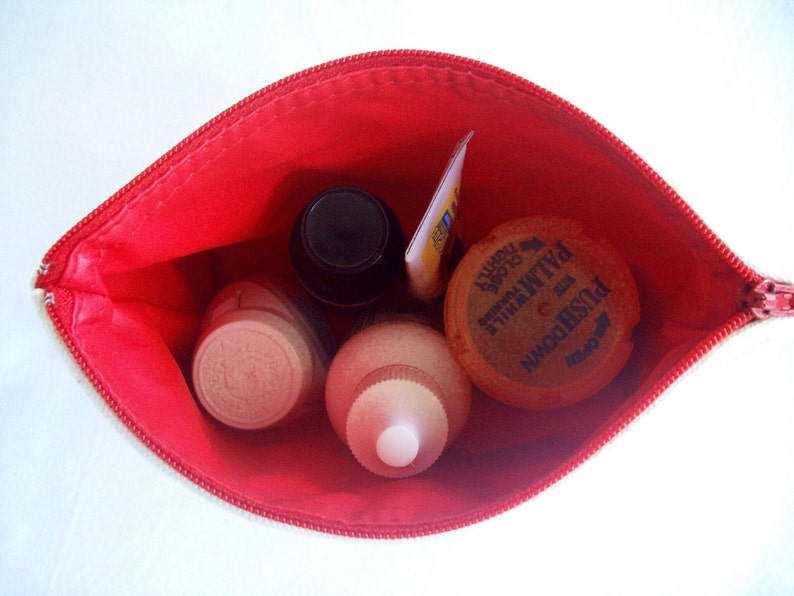 May include: A red zippered pouch with four small bottles and a round container inside. The bottles are clear and contain liquids. The round container is yellow and has blue text that reads "Noodhshed Palmwave"