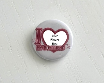 May include: A round, white button with the text "I MY BOYFRIEND" in burgundy. A heart shape in the center has the text "Your Picture Here". The button has a glossy finish and a simple design.