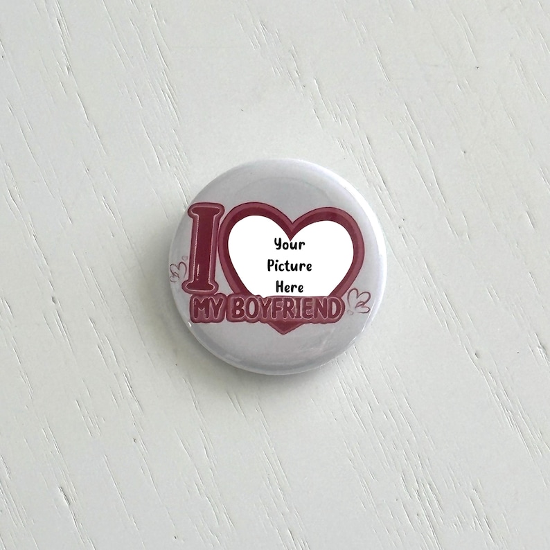 May include: A round, white button with the text "I MY BOYFRIEND" in burgundy. A heart shape in the center has the text "Your Picture Here". The button has a glossy finish and a simple design.