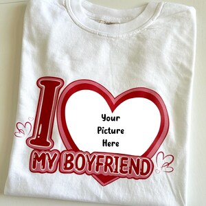 May include: White t-shirt with a red and pink heart design. The shirt features the text "I MY BOYFRIEND" with a space in the heart for a picture. Small heart graphics are on the sides.